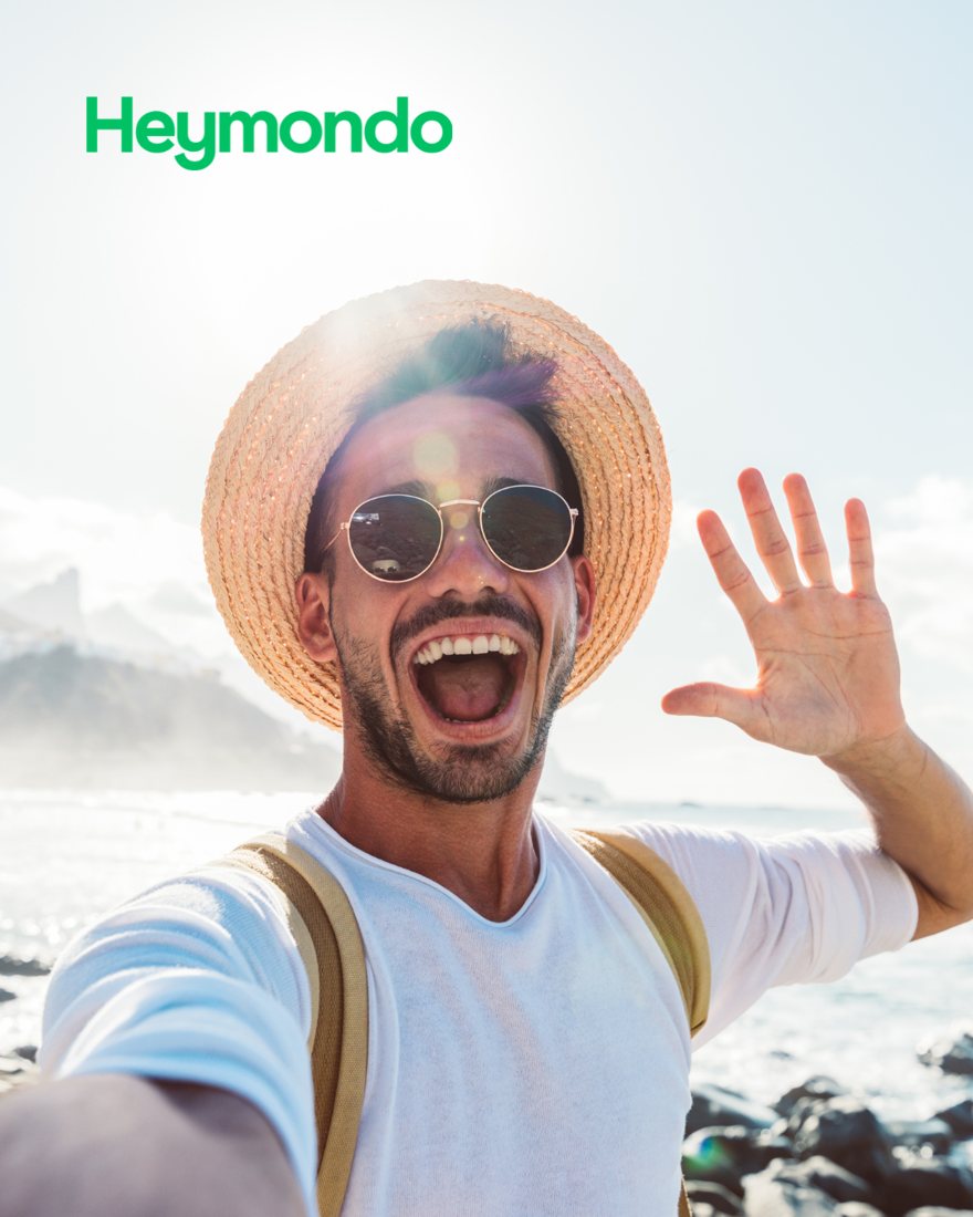 Un voyageur en chapeau de paille qui salue, selfie au bord de la mer, logo Heymondo